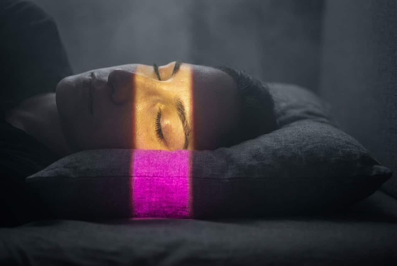 Close-up of a sleeping person with a beam of technicolor light crossing their eyes, illustrating the vivid intensity of cbd dreams and REM rebound.