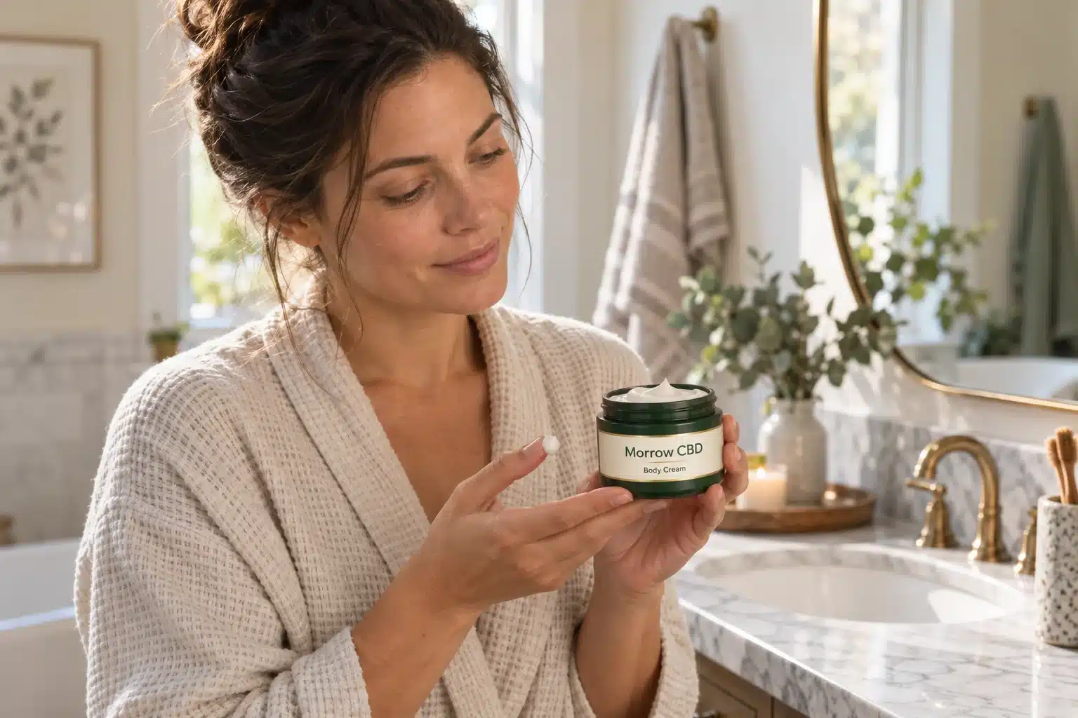 Adult holding a Morrow CBD body cream at a bathroom vanity